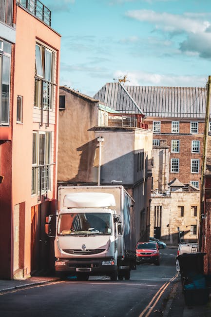 A mobile moving truck from Self Storage Kingston, with an open rear door revealing empty interior space used for house removals and furniture transport, parked on a street next to a red telephone boot