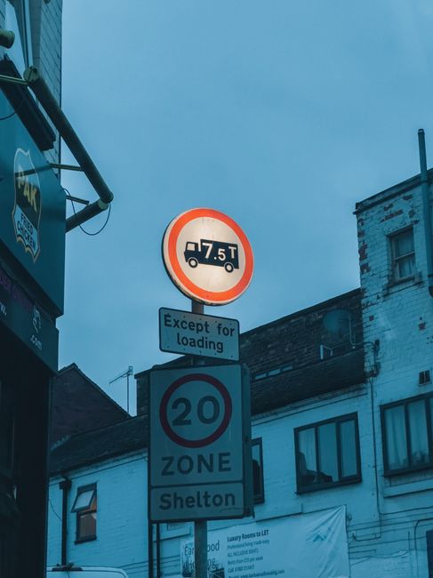 A photograph of a parking area adjacent to a building featuring two no parking signs with a red circle and blue background, each with an 'X' symbol, indicating no stopping except for disabled parking.