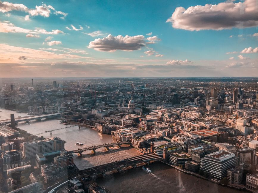A wide view of the Kingston Bridge spanning over the River Thames during an overcast day, with the bridge illuminated by streetlights reflecting on the calm water surface. On the left side of the imag